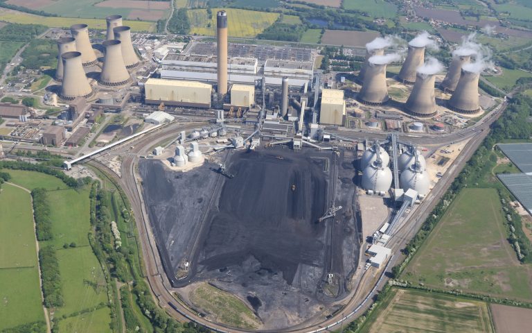 Aerial view of Drax power station, showing a large volume of coal in open storage alongside four spherical biomass storage drums.