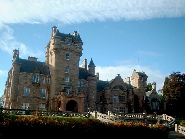 Ardross Castle in the Scottish Highlands, a baronial mansion with turrets, seen from its lawn on a bright day.