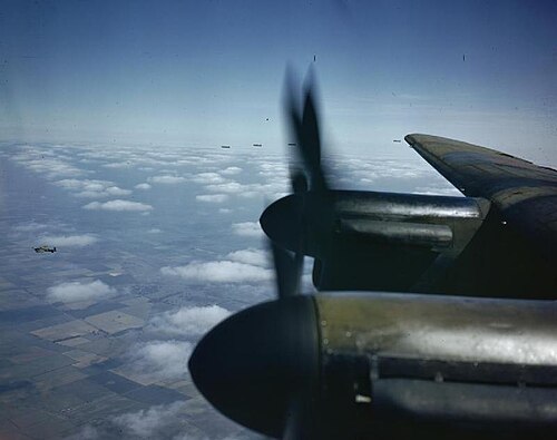 View from a Lancaster cockpit past two propellers, with other Lancaster bombers flying above the clouds.