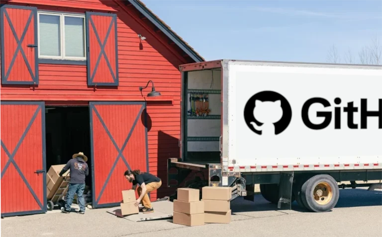 Two people loading cardboard boxes onto a white removals lorry parked outside a red barn.
