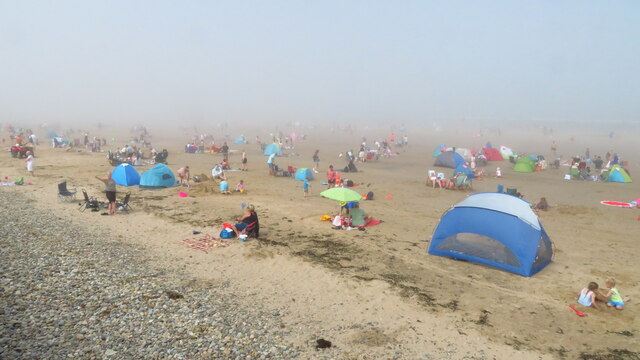 A crowded beach shrouded in grey sea fog, with holidaymakers, beach tents and a lone umbrella fading into the murk.